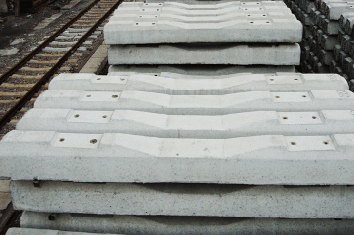 Finished prestressed concrete railway sleepers with fastening insert holes stacked beside track